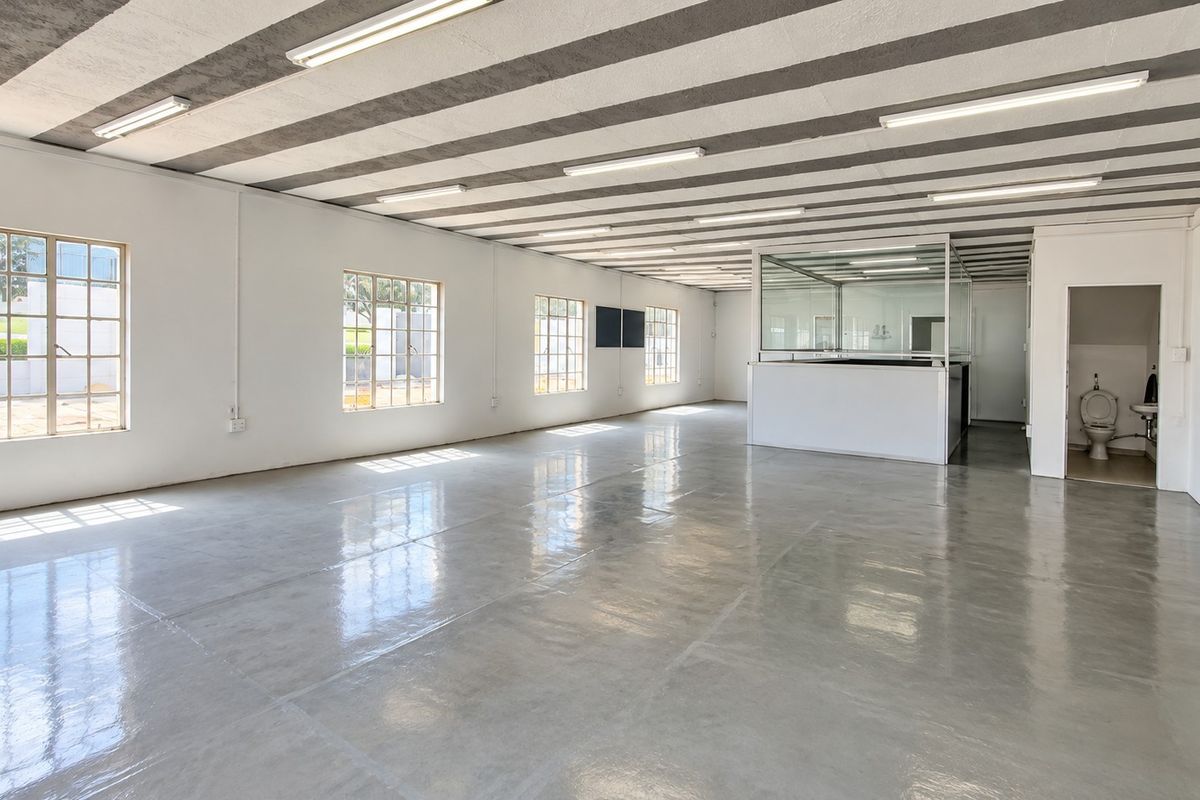 Spacious open-plan retail or office area featuring polished concrete floors, exposed beam ceilings, ample natural light from grid windows, and a private partitioned office space.