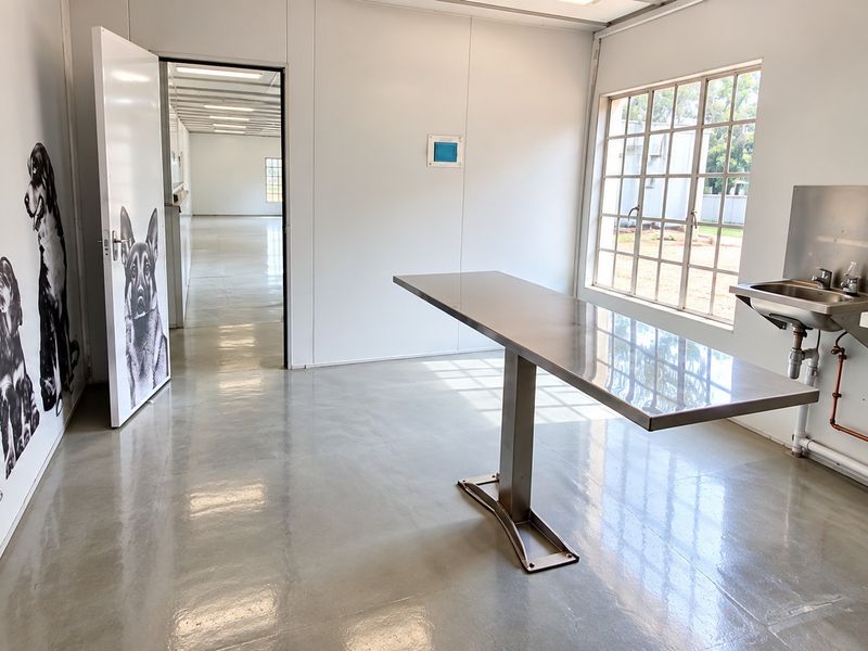 A clean, functional utility space featuring a stainless steel examination table, wall-mounted sink, and polished concrete flooring, suitable for clinical or professional use.