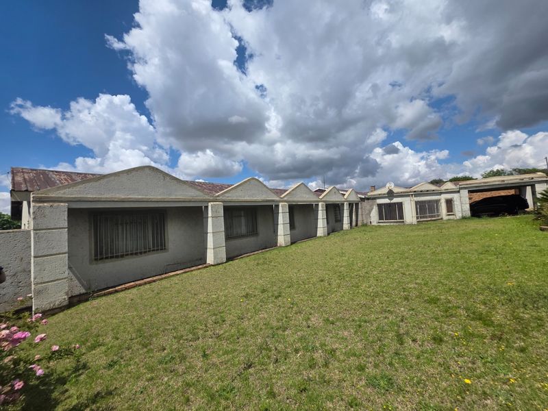 Rear view of the property featuring a distinctive sawtooth roof design, security bars on windows, and a large grass lawn area.