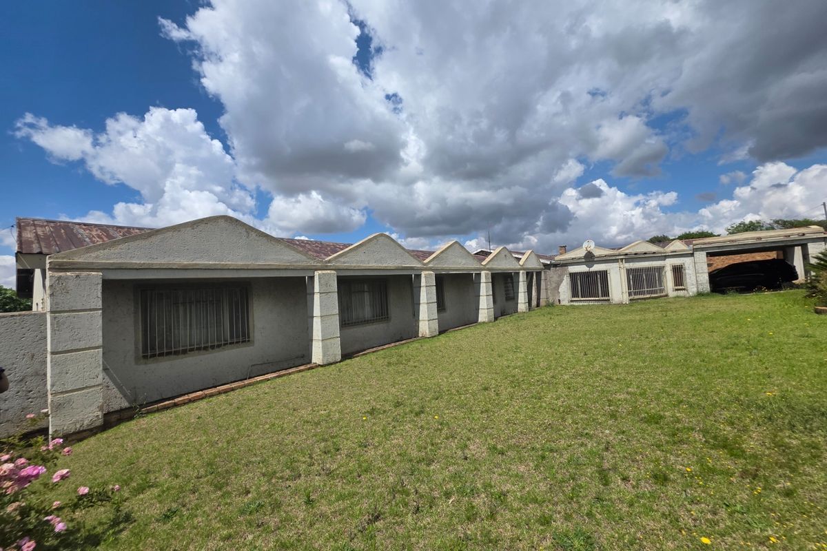 Rear view of the property featuring a distinctive sawtooth roof design, security bars on windows, and a large grass lawn area.