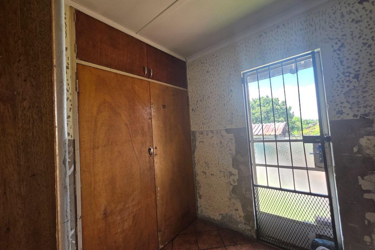 A bedroom featuring built-in wooden cupboards, tiled flooring, and a security gate, currently requiring wall surface repairs and cosmetic updates.