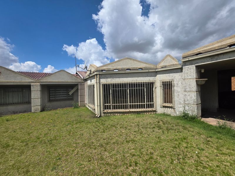 Rear view of the property featuring a plastered facade, security bars on windows, and a lawn area requiring maintenance.