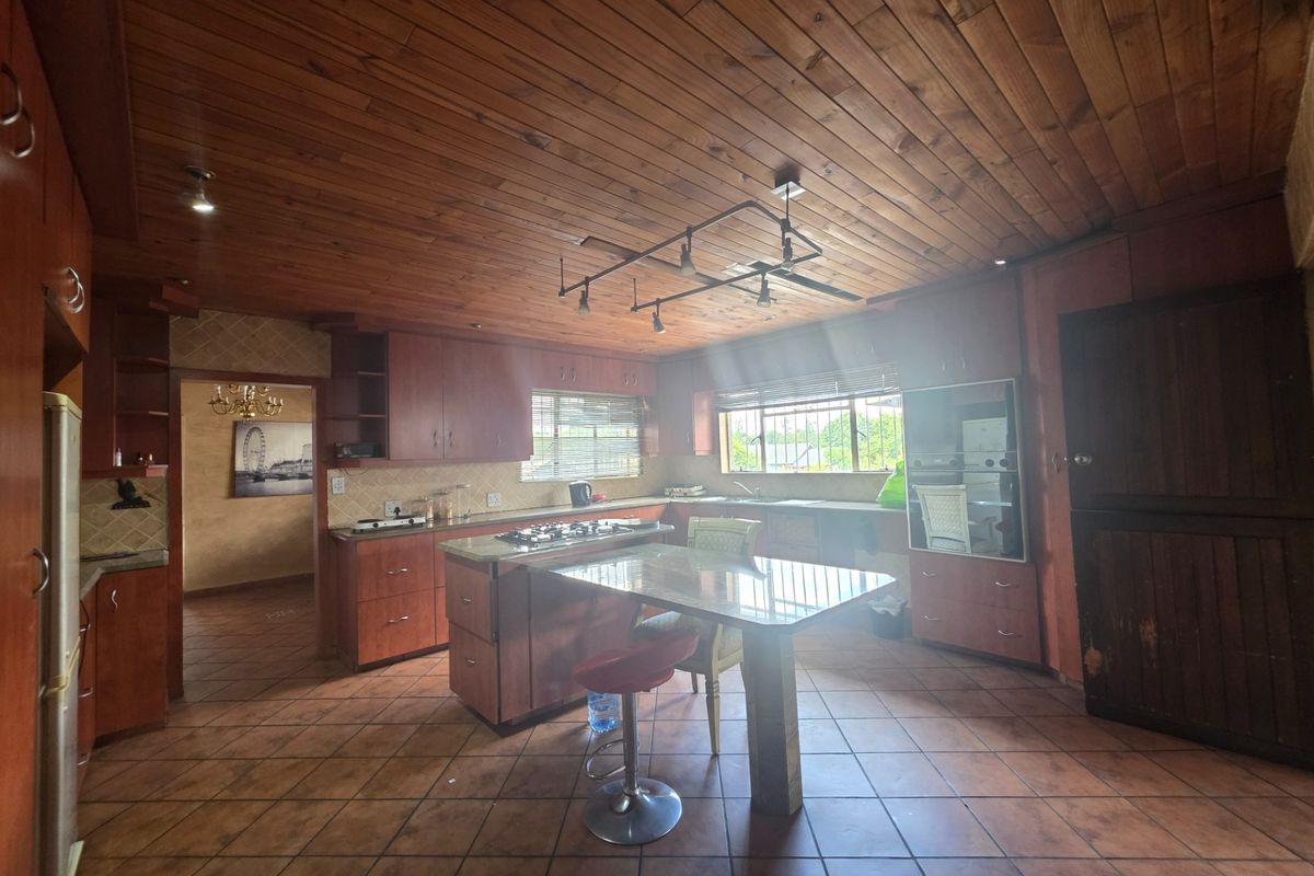 Spacious kitchen featuring extensive wooden cabinetry, a central island with a gas hob, tiled flooring, and a distinctive wooden panelled ceiling.