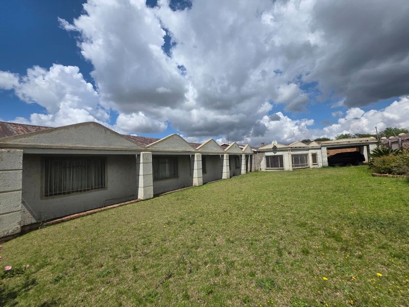 Rear view of the property featuring a large lawn, security bars on windows, concrete pillars, and an attached carport area.