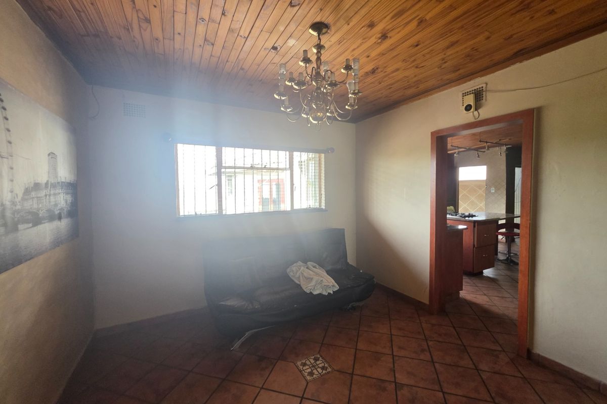 A living area featuring terracotta floor tiles and a timber tongue and groove ceiling, with a view through to the adjacent kitchen area.