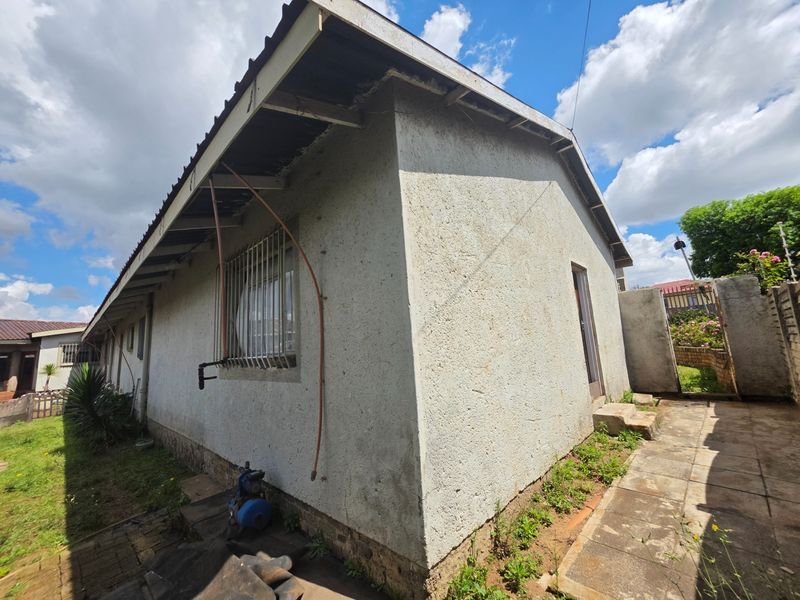 Rear exterior view of the house showing textured plaster walls, security bars on windows, and a paved walkway with a water pump.