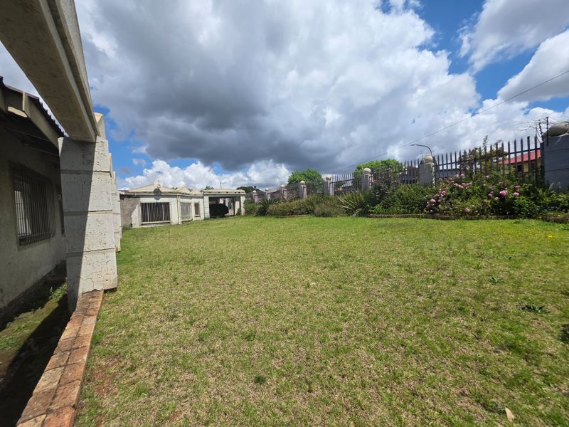 A spacious rear garden area featuring a lawn, perimeter metal security fencing with brick pillars, and views of the rear building elevation.