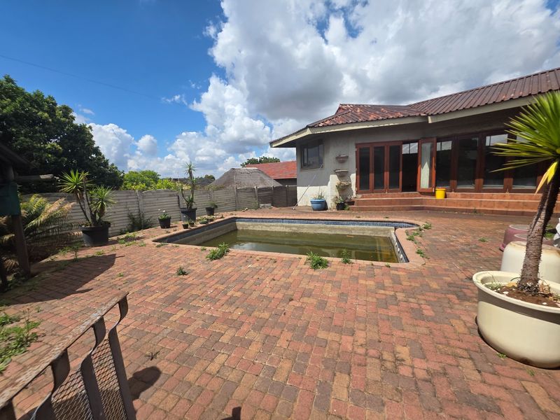 Outdoor pool area featuring a brick-paved patio and direct access to the house through timber-framed glass doors, requiring maintenance and pool restoration.