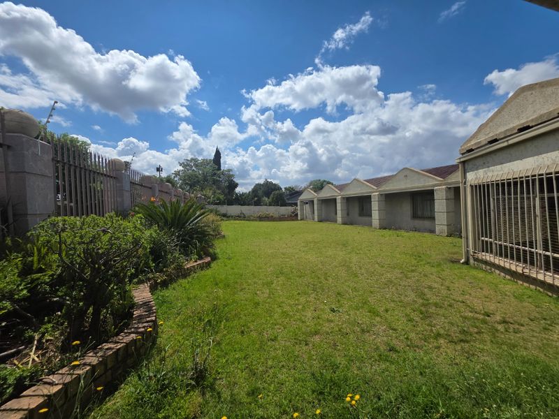 A spacious rear garden area featuring a lawn, brick garden edging, and secure perimeter fencing with window security bars on the building exterior.