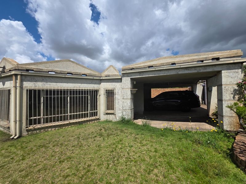 Front elevation of the property featuring a built-in carport, security bars on windows, and a concrete facade requiring maintenance.