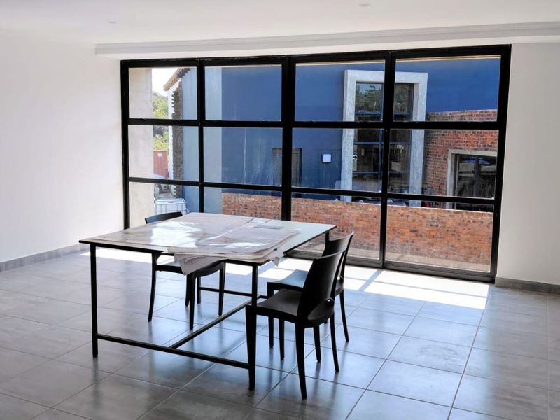 A bright, modern office space featuring large black-framed grid windows, neutral tiled flooring, and a clean, minimalist aesthetic suitable for a professional workspace.