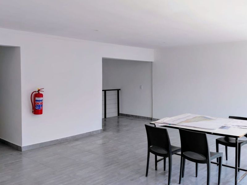 A bright, open-plan commercial office space featuring neutral white walls, grey tiled flooring, and a wall-mounted fire extinguisher.