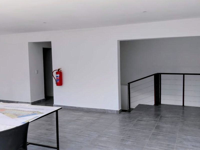 A bright, open-plan commercial office space featuring modern grey floor tiles, a staircase with a metal railing, and a wall-mounted fire extinguisher.