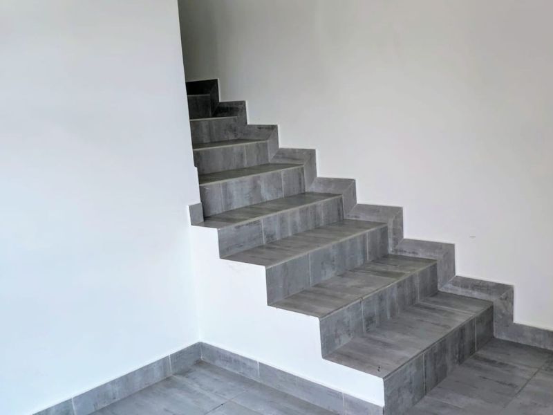 A clean, modern interior space featuring a tiled staircase with grey wood-look tiles and white walls.