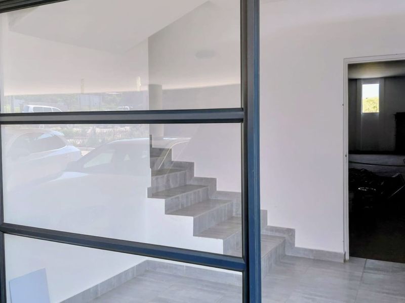 Modern entrance area featuring a tiled staircase, large glass panel window, and clean neutral finishes, leading into an open interior space.