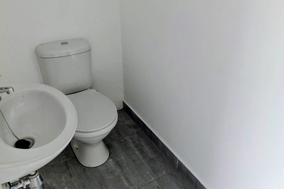 A compact bathroom featuring a pedestal sink, a standard toilet, and modern grey tiled flooring.
