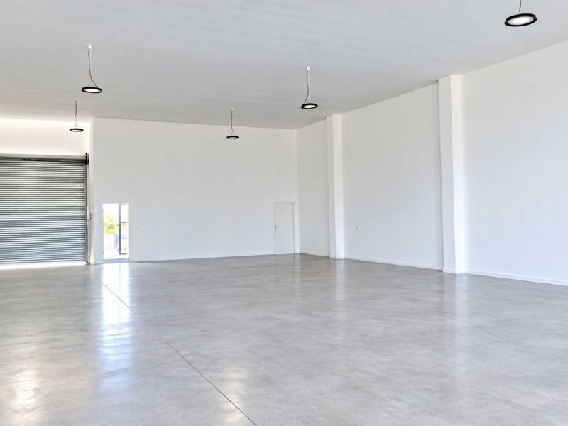 A spacious, modern open-plan commercial unit featuring polished concrete floors, high ceilings, and a large roller shutter door for convenient access.