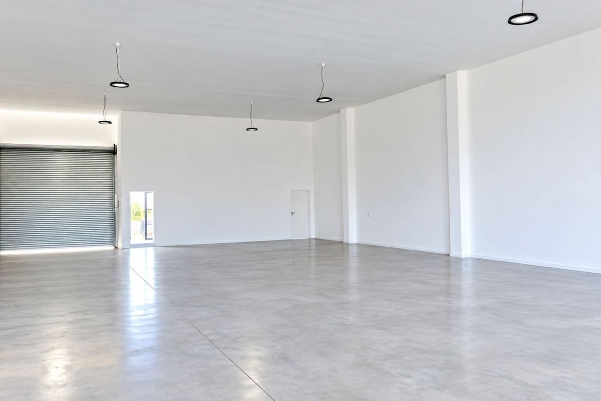 A spacious, modern open-plan commercial unit featuring polished concrete floors, high ceilings, and a large roller shutter door for convenient access.