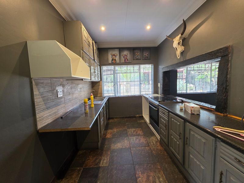 A galley-style kitchen featuring dark cabinetry, tiled flooring, built-in oven and hob, and a tiled backsplash with security bars on the windows.