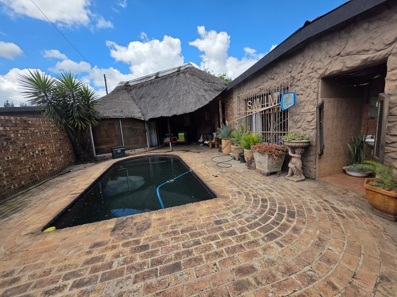 Outdoor pool area featuring a swimming pool, brick paved surround, and a thatched roof structure, providing a rustic entertainment space.
