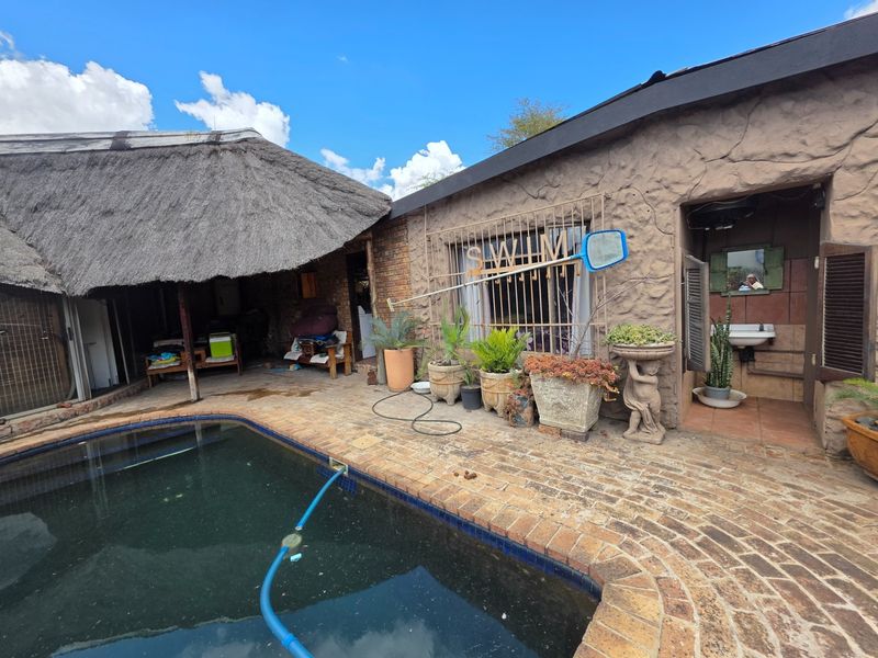Outdoor pool area featuring a thatched roof structure, brick paving, and a rustic stone-textured exterior wall with an integrated outdoor basin.
