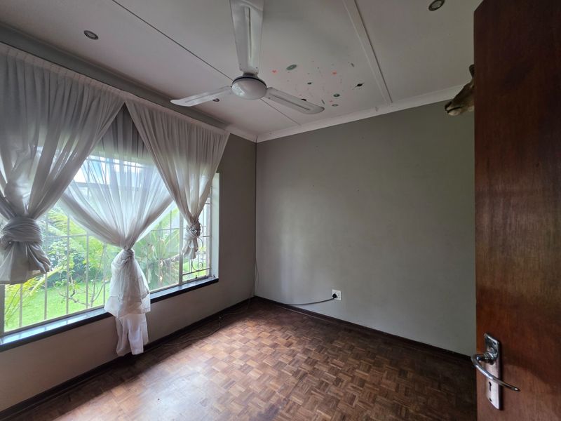 An empty bedroom featuring parquet flooring, a ceiling fan, and security bars on the window, offering a blank canvas for personalization.