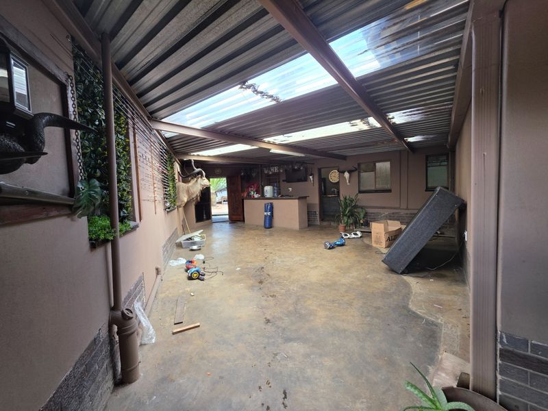 A covered outdoor patio area featuring a built-in bar counter, concrete flooring, and a corrugated metal roof with translucent panels for natural light.