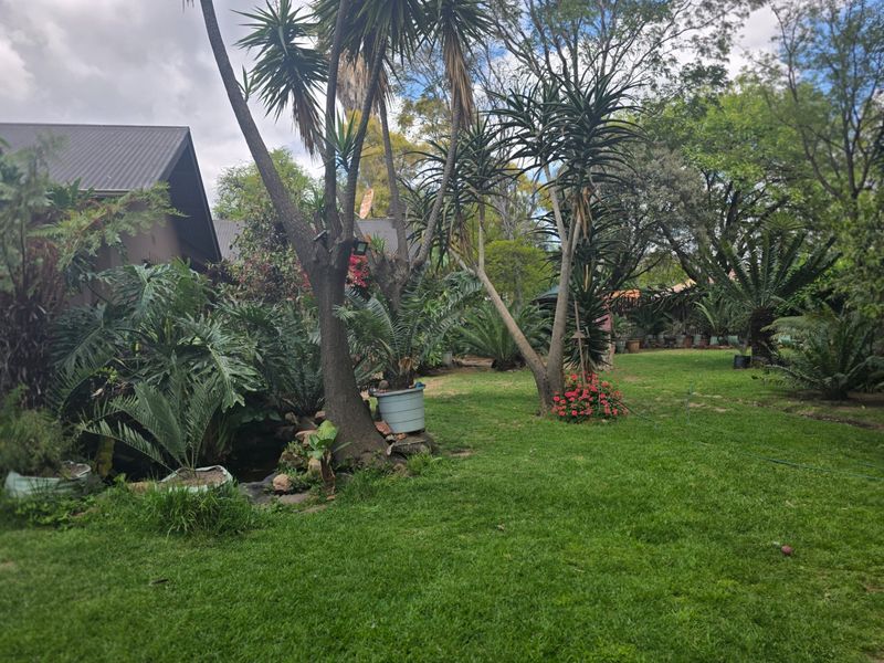 A lush, well-established garden featuring mature trees, diverse plantings, and a spacious lawn area, providing a serene outdoor environment.