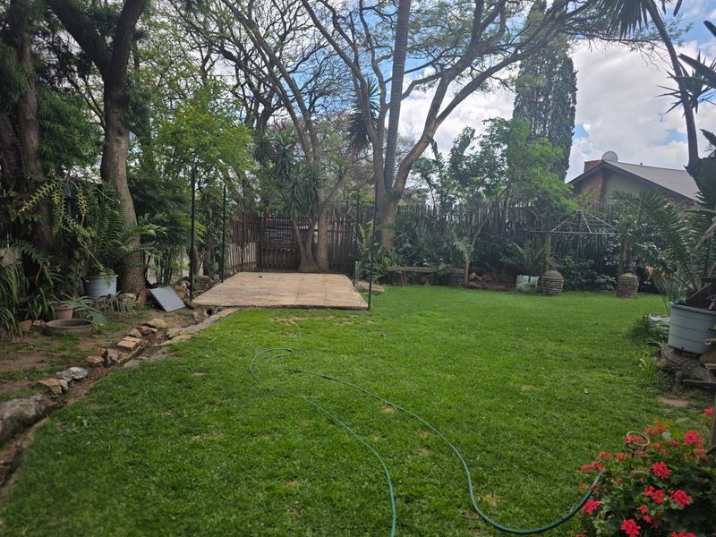 A spacious backyard garden featuring a paved patio area, established mature trees, and a lawn, offering potential for outdoor landscaping and entertainment space.