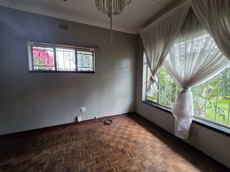 An empty bedroom featuring classic parquet flooring, security bars on windows, and neutral wall tones, offering a blank canvas for personalization.