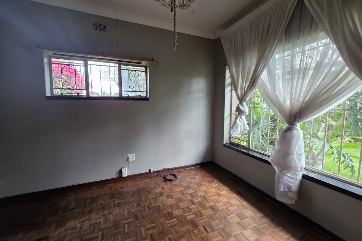 An empty bedroom featuring classic parquet flooring, security bars on windows, and neutral wall tones, offering a blank canvas for personalization.