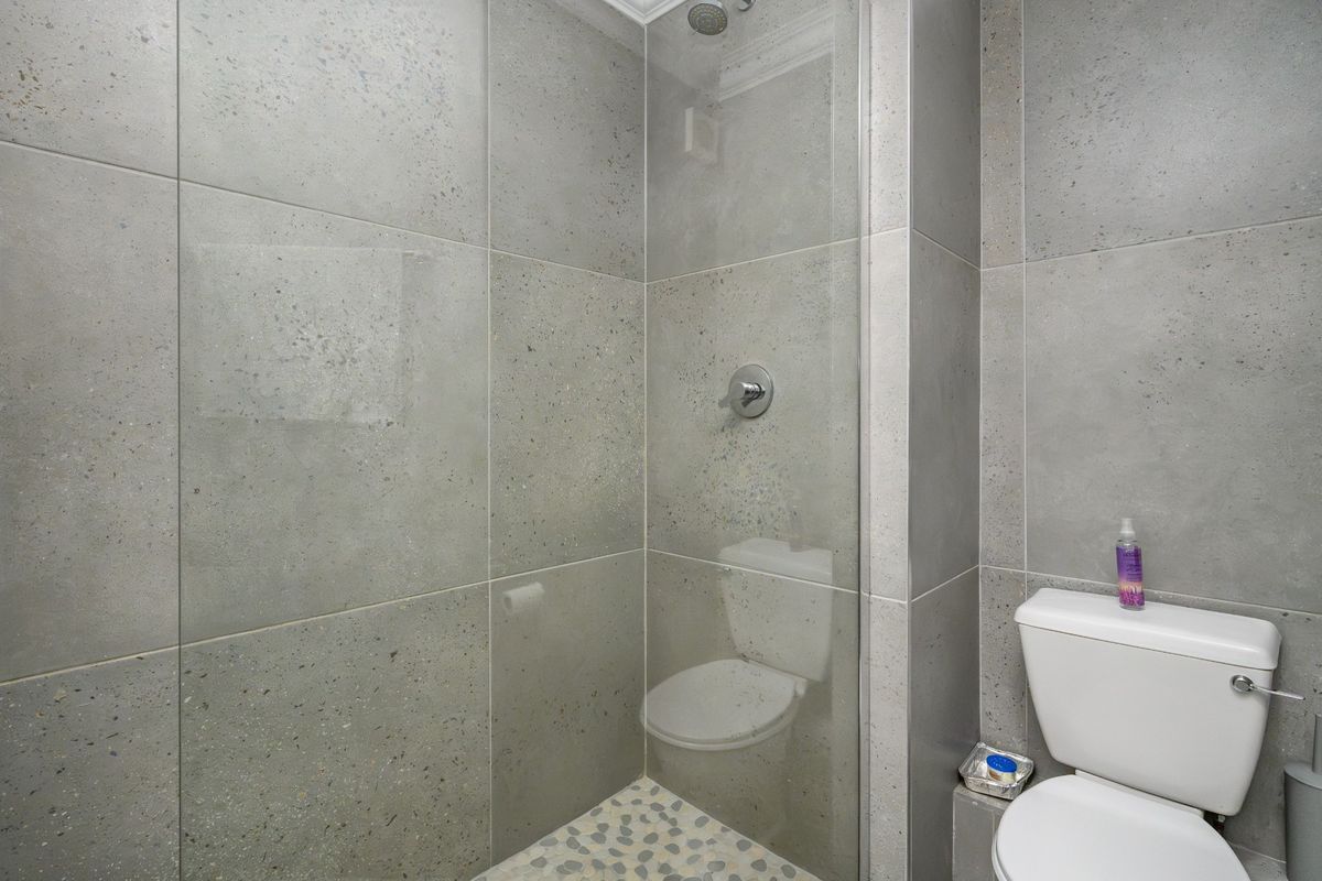 Modern bathroom featuring a walk-in shower with glass screen, pebble tile flooring, and neutral grey wall tiles.