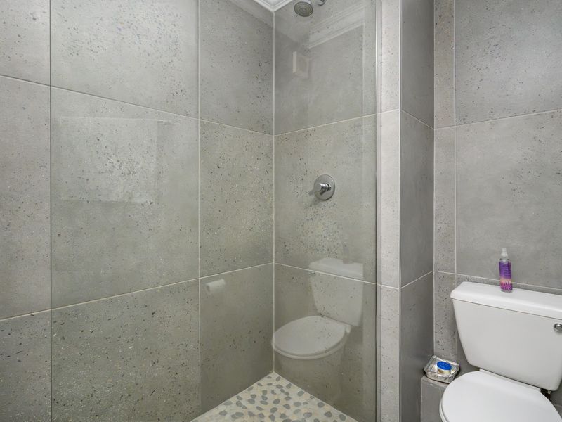 Modern bathroom featuring a walk-in shower with glass screen, pebble tile flooring, and neutral grey wall tiles.