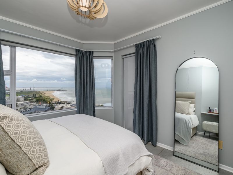 A bright bedroom featuring large bay windows with panoramic coastal views, neutral wall finishes, and coving detail.