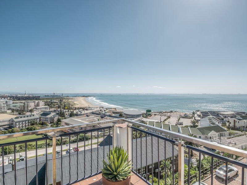 A balcony featuring metal railings and tiled flooring, offering expansive coastal and urban views.