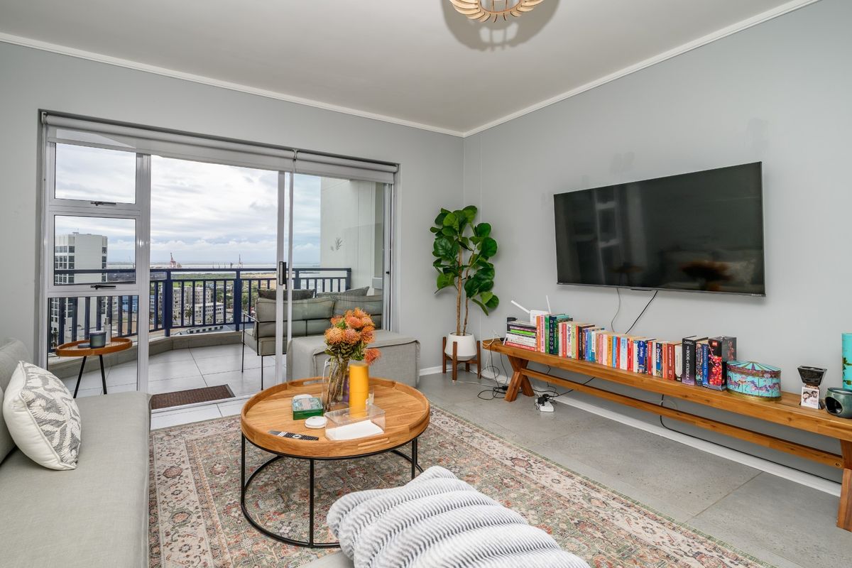A bright living room featuring tiled flooring and large sliding glass doors that open onto a private balcony with city views.