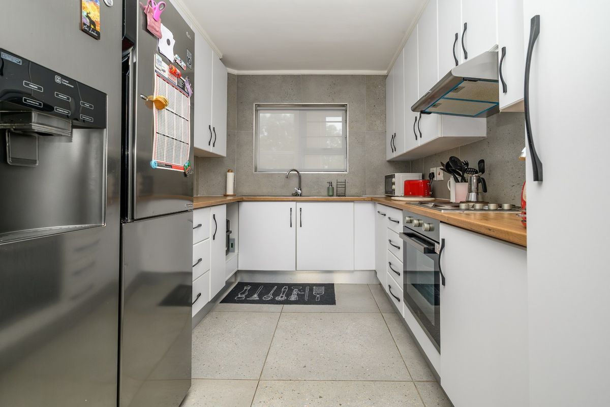 A modern, well-maintained kitchen featuring white cabinetry, wooden countertops, stainless steel appliances, and neutral tiled flooring.