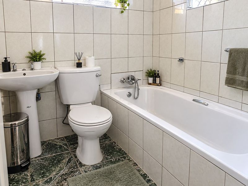 A functional bathroom featuring a pedestal basin, standard toilet, and a bathtub with wall-to-wall tiling and patterned floor tiles.
