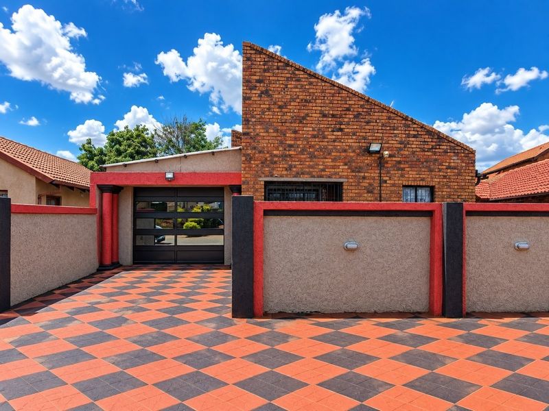 Front exterior view of the property featuring a distinctive brick facade, a modern garage door, and a patterned paved driveway with boundary walls.