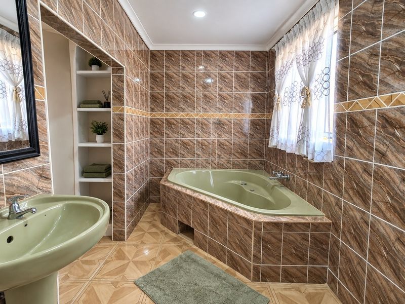 A bathroom featuring a corner bathtub, pedestal basin, and floor-to-ceiling tiled walls with built-in shelving.