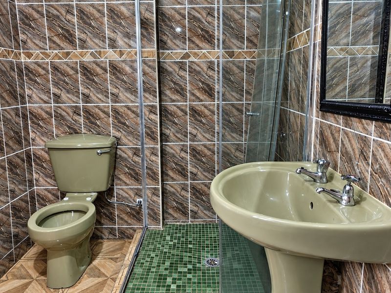 A dated bathroom featuring olive-toned sanitaryware, a glass shower enclosure, and full-height decorative wall tiling.