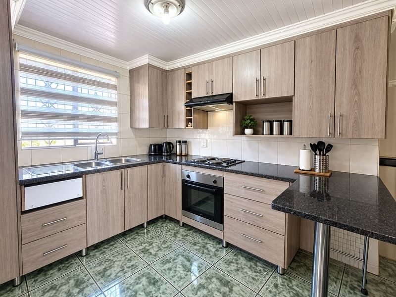 Modern kitchen featuring wood-look laminate cabinetry, granite countertops, built-in oven with gas hob, and tiled flooring throughout.