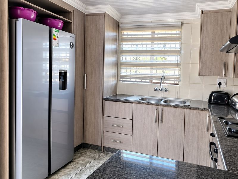 Modern kitchen featuring light wood-grain cabinetry, granite countertops, a double sink, and integrated hob with extractor fan.