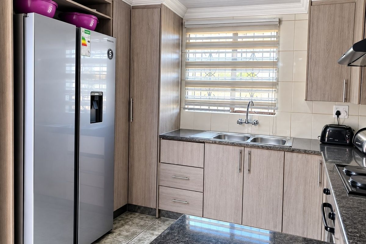 Modern kitchen featuring light wood-grain cabinetry, granite countertops, a double sink, and integrated hob with extractor fan.