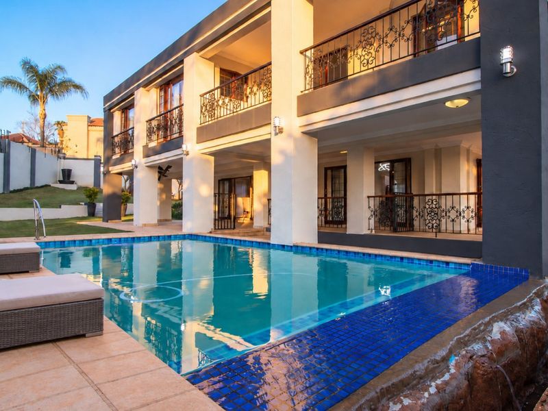 A well-maintained swimming pool area featuring a stone water feature, tiled surround, and a spacious covered patio with decorative wrought iron railings.