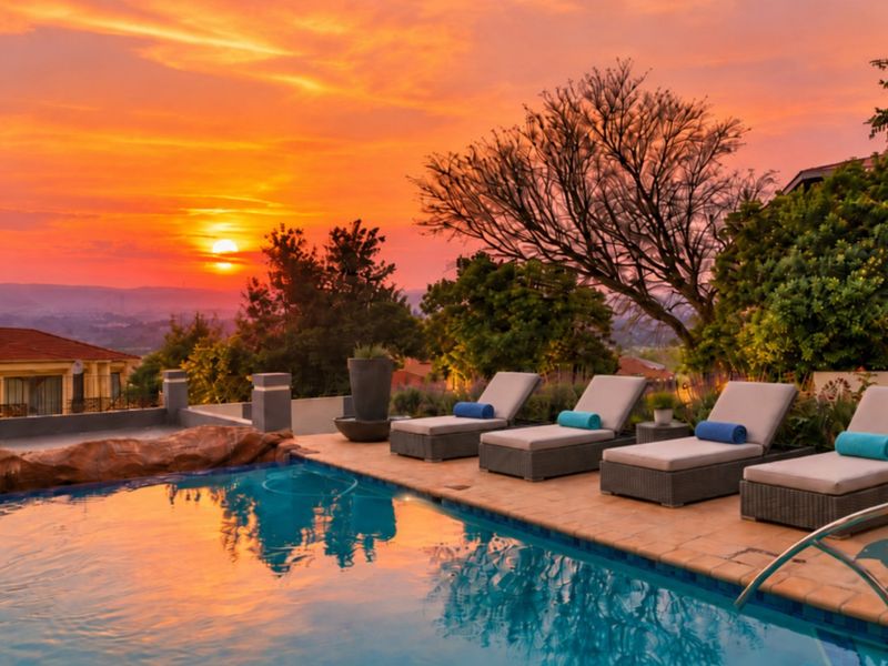 A beautifully landscaped pool area featuring a rock-accented swimming pool and paved deck, perfectly positioned to enjoy stunning sunset views.