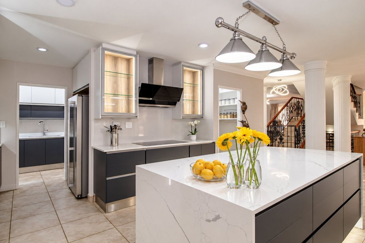 Modern kitchen featuring a large central island with quartz countertops, sleek cabinetry, integrated appliances, and an adjacent scullery area.