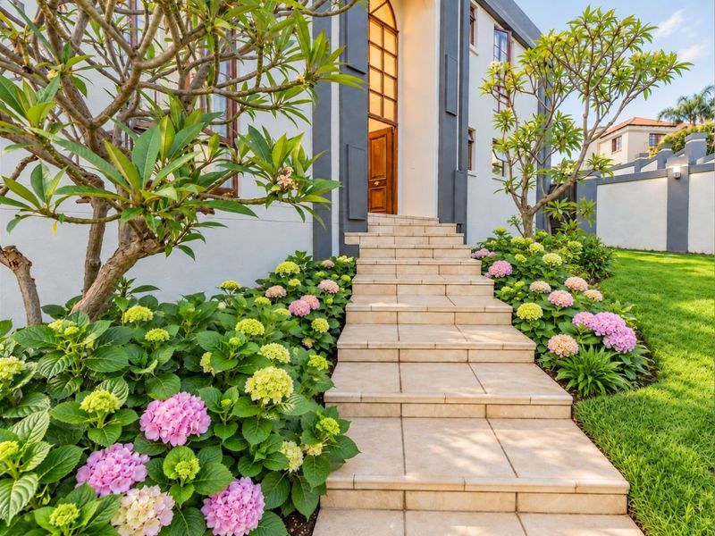 A well-maintained front entrance featuring a tiled staircase leading to an arched doorway, surrounded by lush, manicured garden beds.