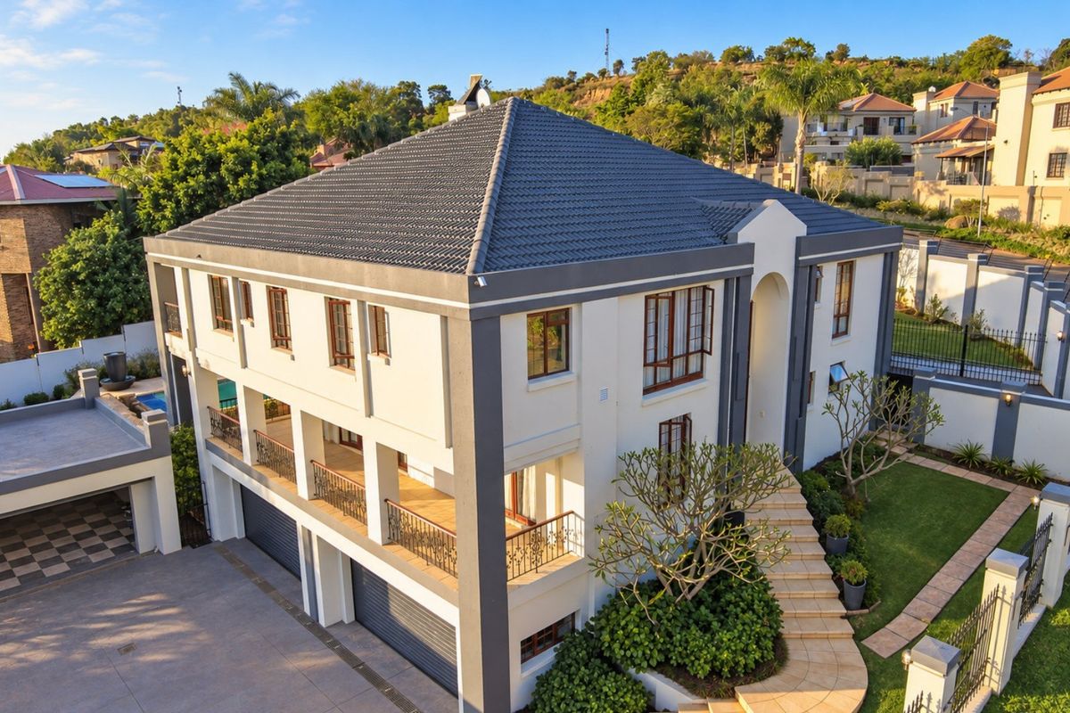 Aerial view of a modern multi-story residential property featuring a tiled roof, double garage, spacious balconies with iron railings, and a well-maintained garden.