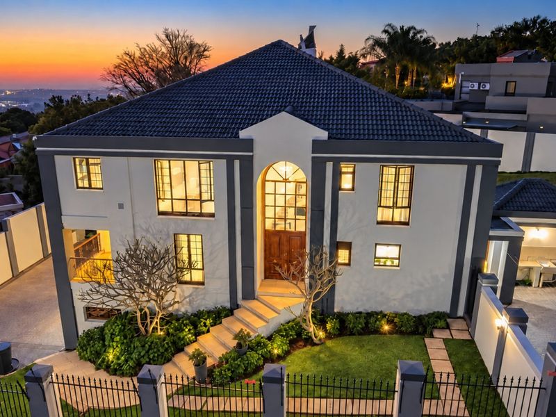 Stunning double-storey residence featuring a striking arched entrance, modern exterior finishes, manicured garden, and secure perimeter fencing, captured at twilight.